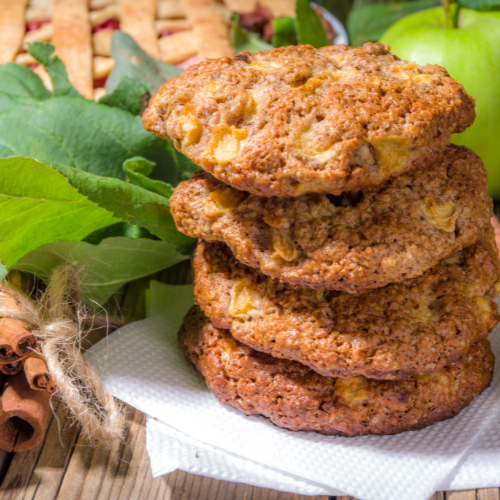 Indulge in delightful apple pie cookies in a stack, warm from the oven. on the counter next to a bundle of cinnamon sticks and a granny smith apple.